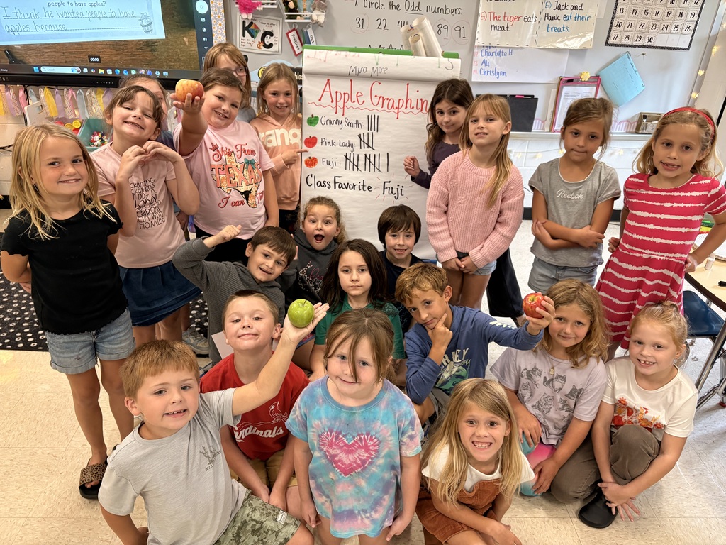 Elementary students pose around an “Apple Graphing” chart showing Fuji as the class favorite, with several children holding apples.