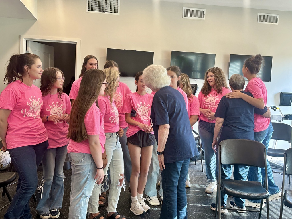 Volleyball players in matching pink shirts mingle and share hugs with older adults after a group activity.