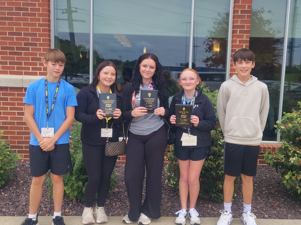 Five students pose outside a brick building; three hold leadership award plaques and wear event badges.