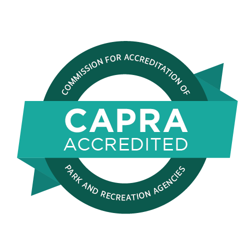 CAPRA logo with a green banner that says "CAPRA ACCREDITED" and a dark green circle around it with the words "Commission for Accreditation of Park and Recreation Agencies"