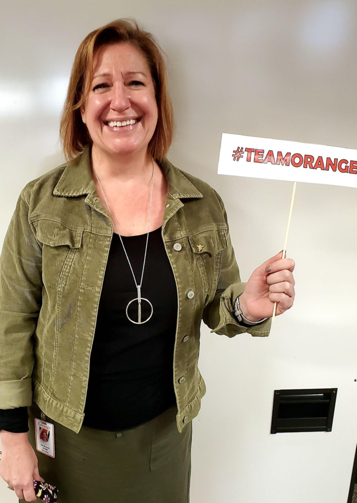 A woman smiling at the camera and holding a "team orange" sign