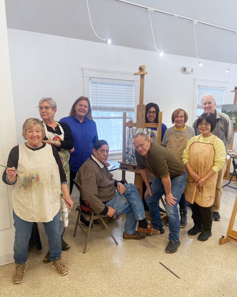 A group of artists standing around an easel and smiling at the camera