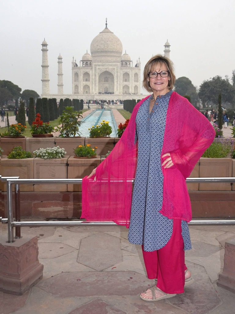 A woman standing in front of the Taj Mahal in pink and blue clothing, smiling at the camera