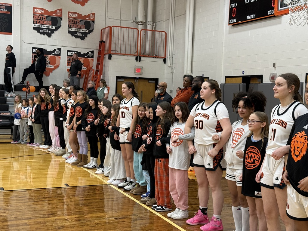 A group of student basketball players lined up on one side of a basketball court with arms hooked around each other