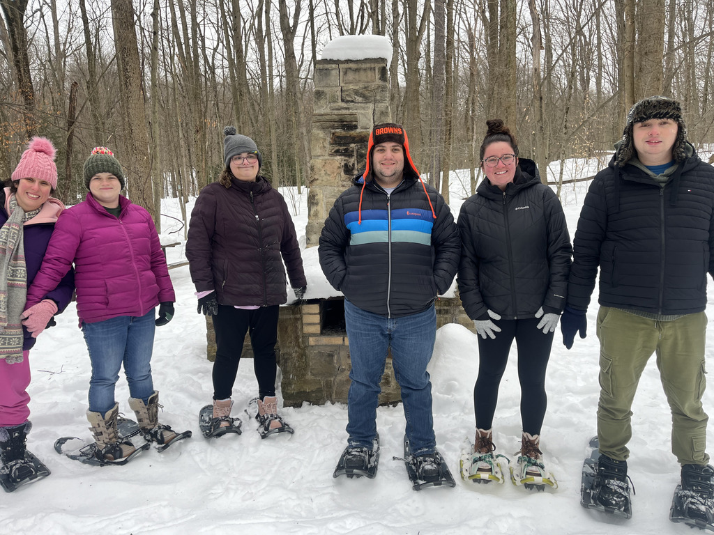 A group of participants in showshoes, hats, coats, scarves, and boots getting ready to snowshoe