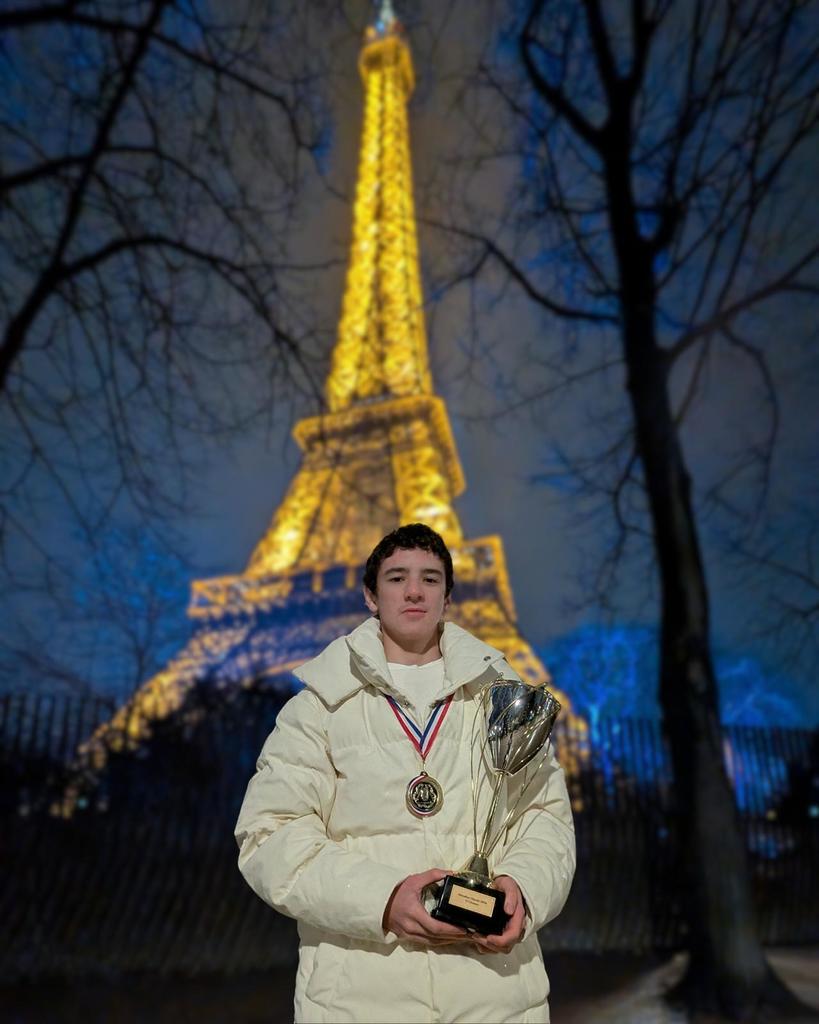 A student athlete holds a trophy and stands in front of the Eiffel Tower in Paris 