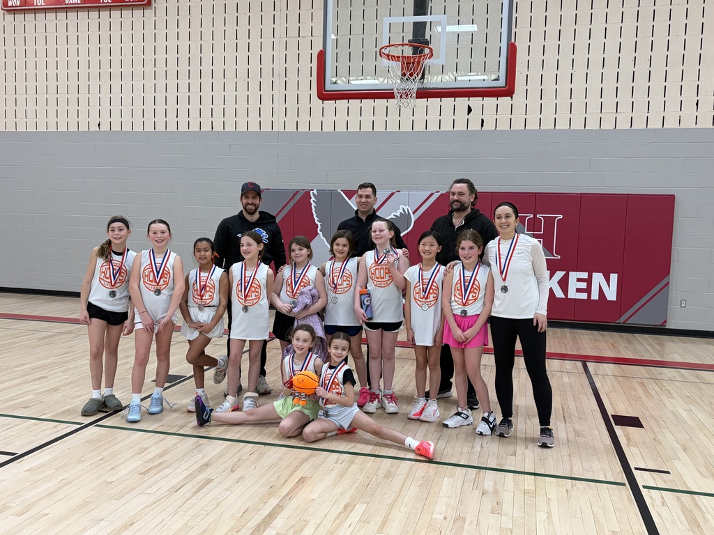 A group of basketball girl players wearing medals around their necks and smiling at the camera