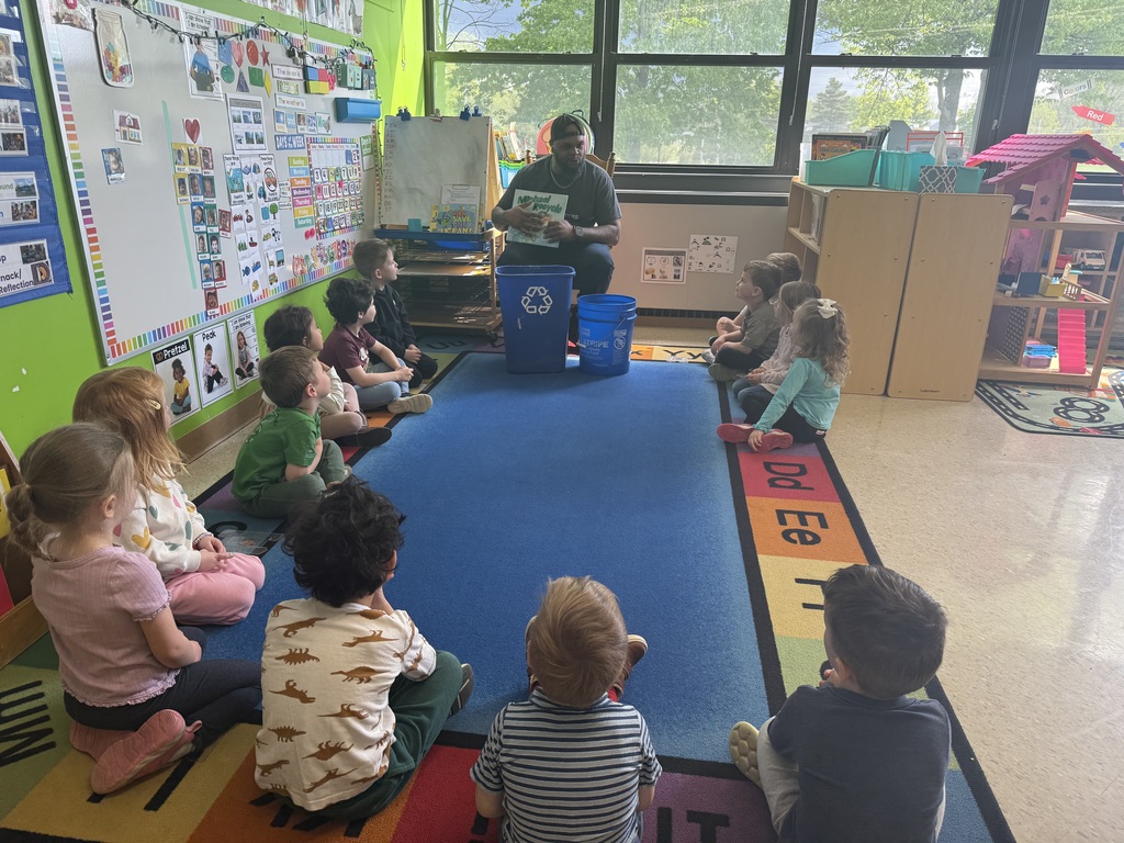 A group of preschool students listen to a book read by Mr. Mike 