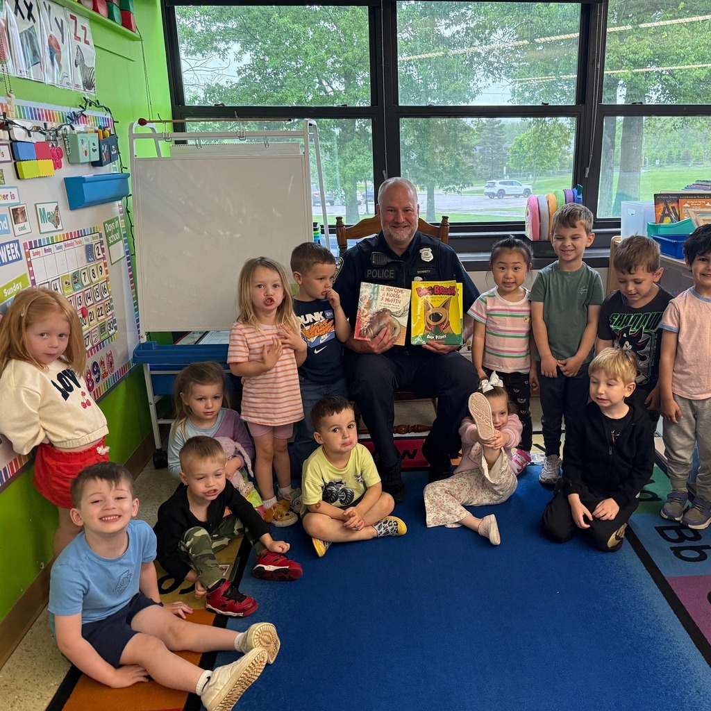 A group of preschoolers gather around a police officer, who is holding children's books