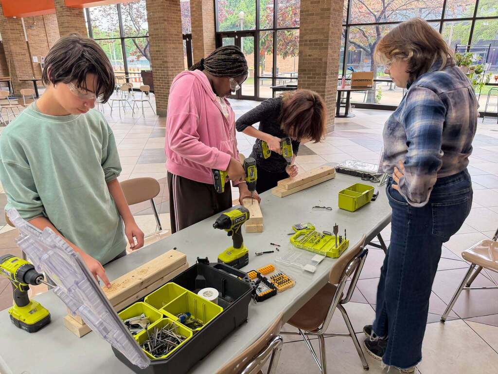 A few students work with drill tools, standing around a table 