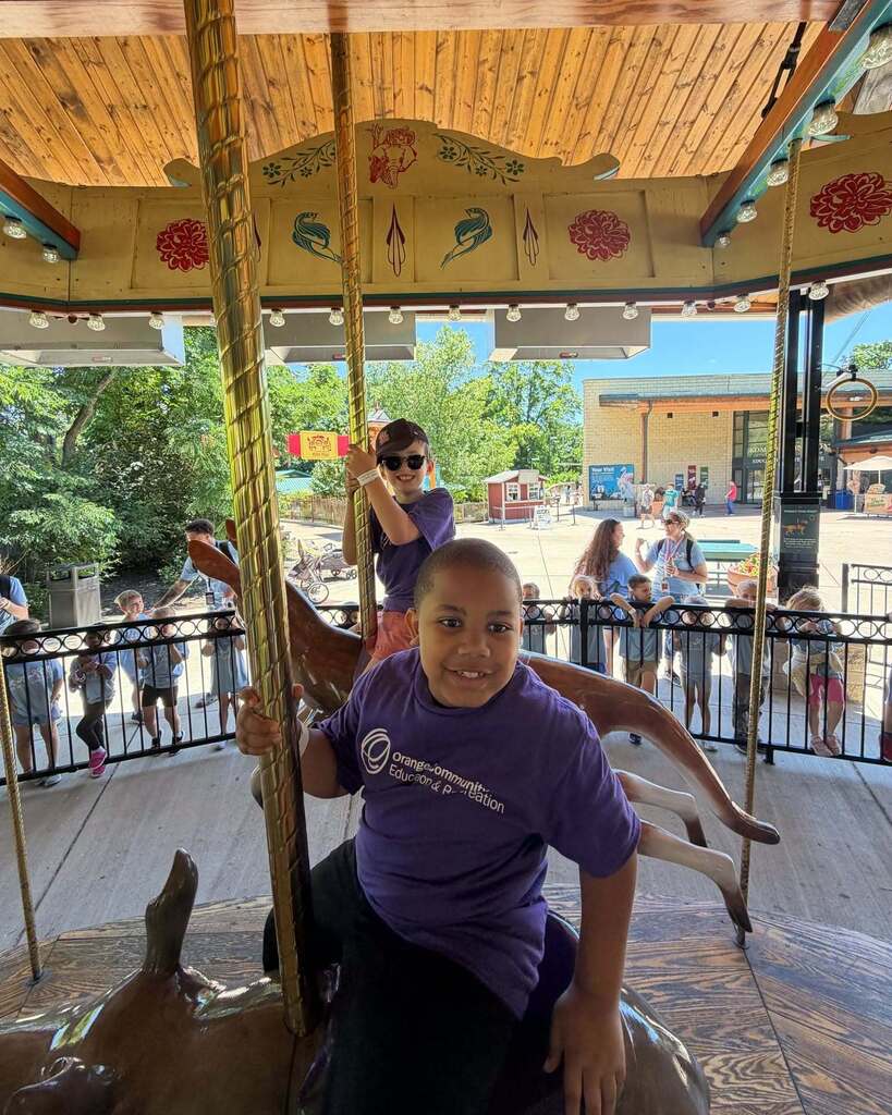 Two students ride a merry go round and smile at the camera