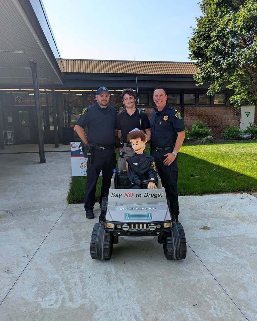 Three police officers pose with a remote control police car and smile at the camera