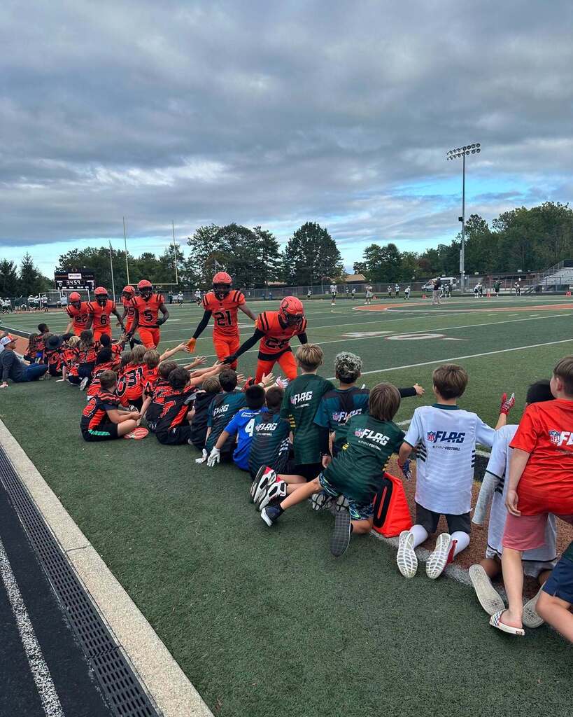 A group of high school football players running on the sidelines and high fiving young football players
