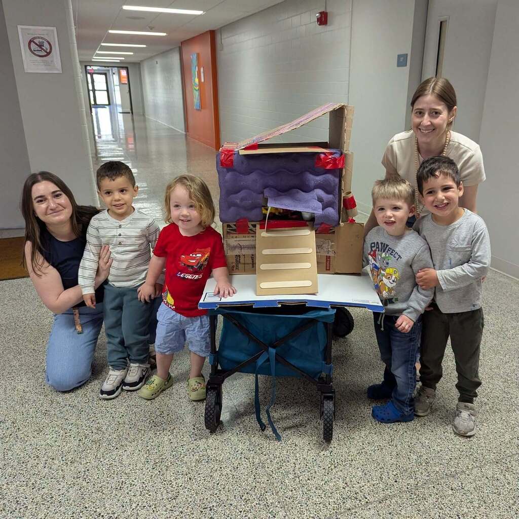 A couple preschool teachers with some preschool students around a homemade chicken coop