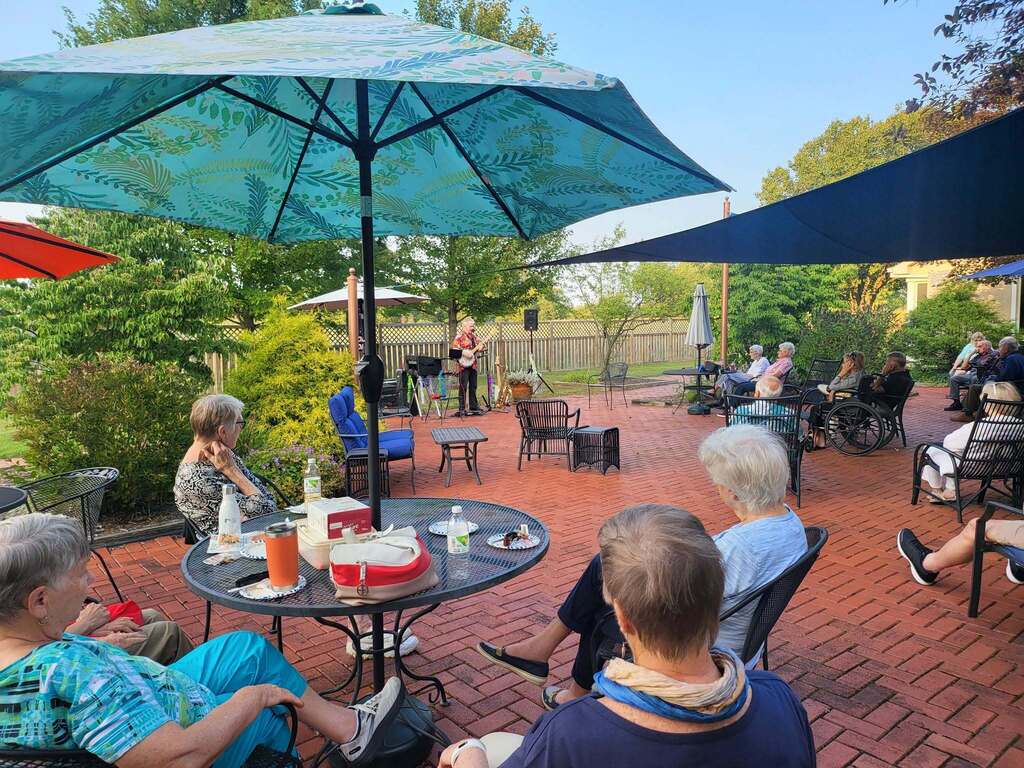A group of people sit outside on a patio and listen to a live musician