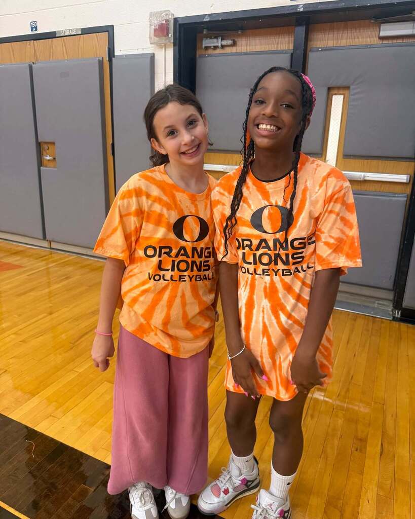Two girls wearing orange tie-dye "Orange Lions Volleyball" shirts smiling and looking at the camera