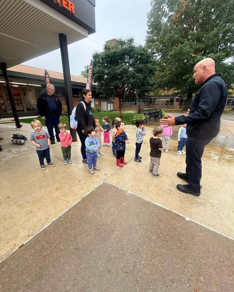 A group of preschoolers stand outside the Pepper Pike Learning Center listening to a police officer talking to them