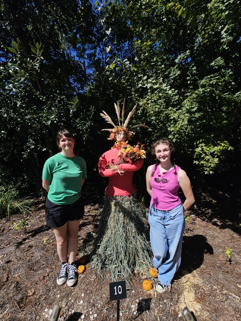 two students standing next to the scarecrow