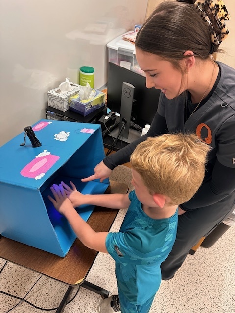 OHS student with child with hands under blue light