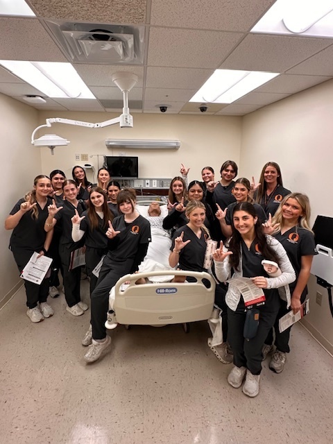 students around hospital bed with Lamar hand sign