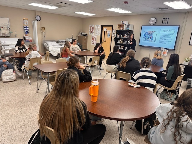 students sitting at tables while a speaker presents