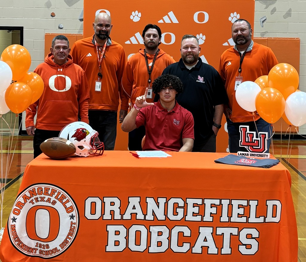 student sitting in red shirt with coaches standing around him in orange and black shirts