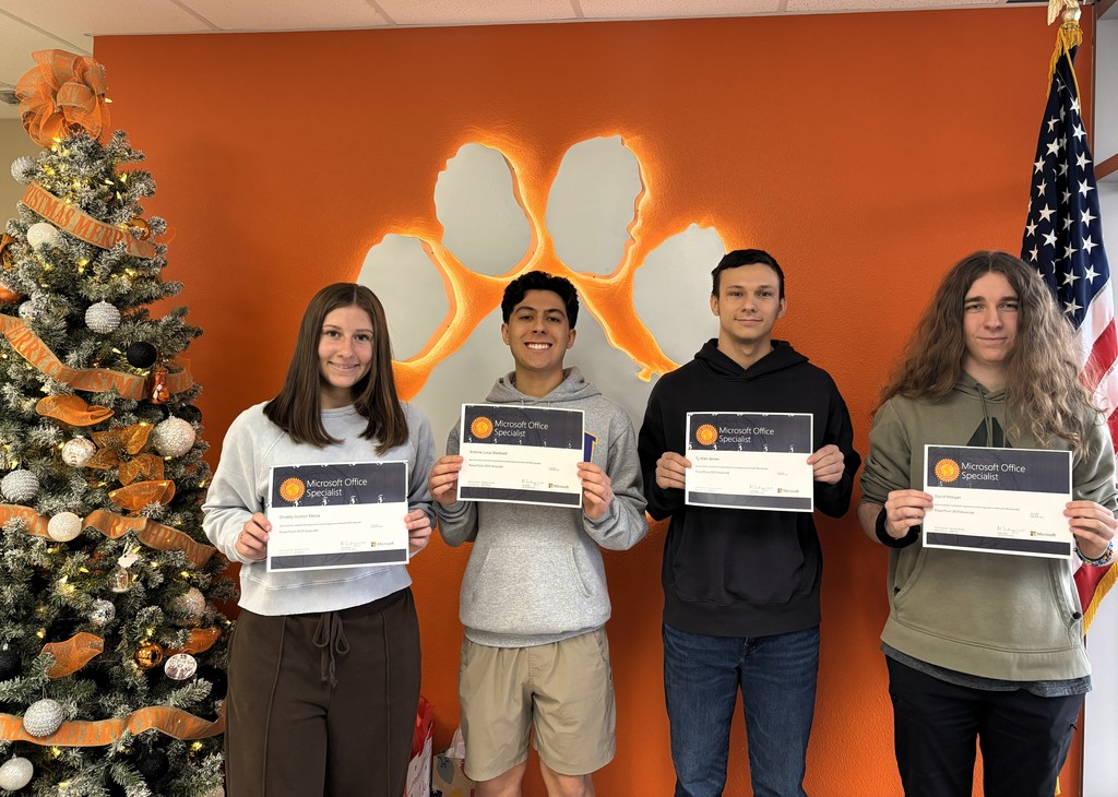 four students holding certification papers in front of an orange wall with a white paw