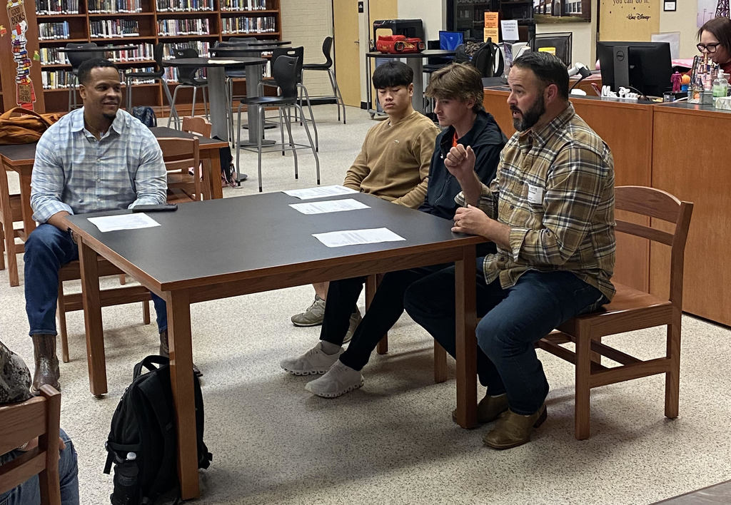 two men and two students sitting at a table in a library