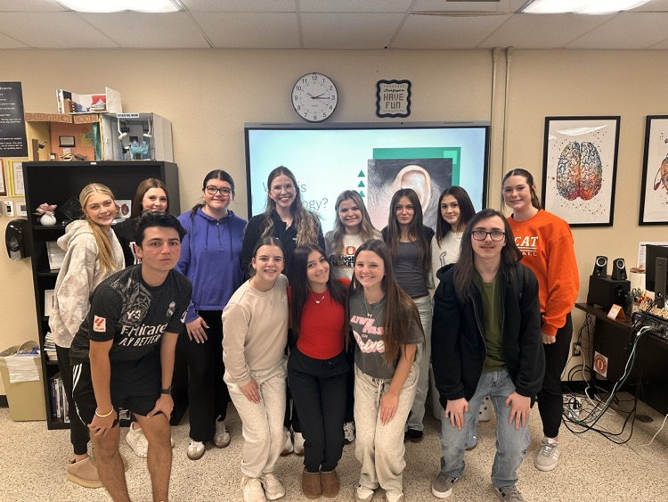 several students standing in a classroom around a guest speaker