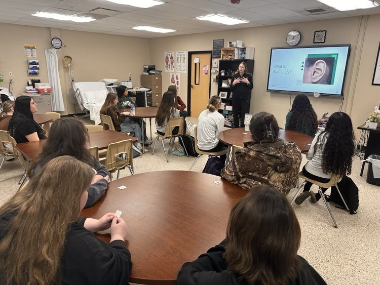 students sitting at a table listening to a guest speaker