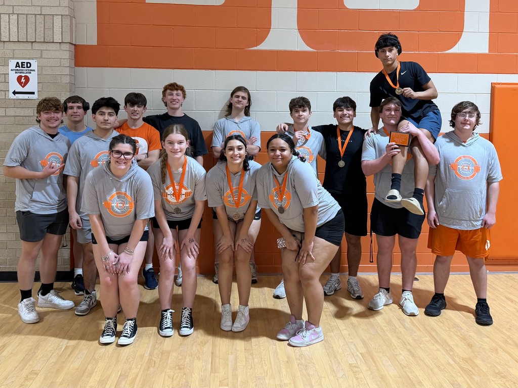 A group of students in matching shirts and shorts pose for a photo in a gym.