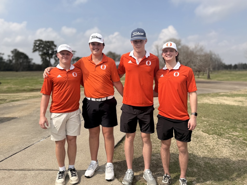 Four men in orange shirts and caps stand on a golf course path, smiling and posing for a photo.