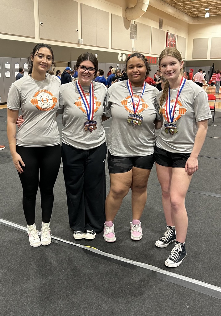 Four young women in matching gray T-shirts, black pants, and sneakers, standing in a gym with medals around their necks.