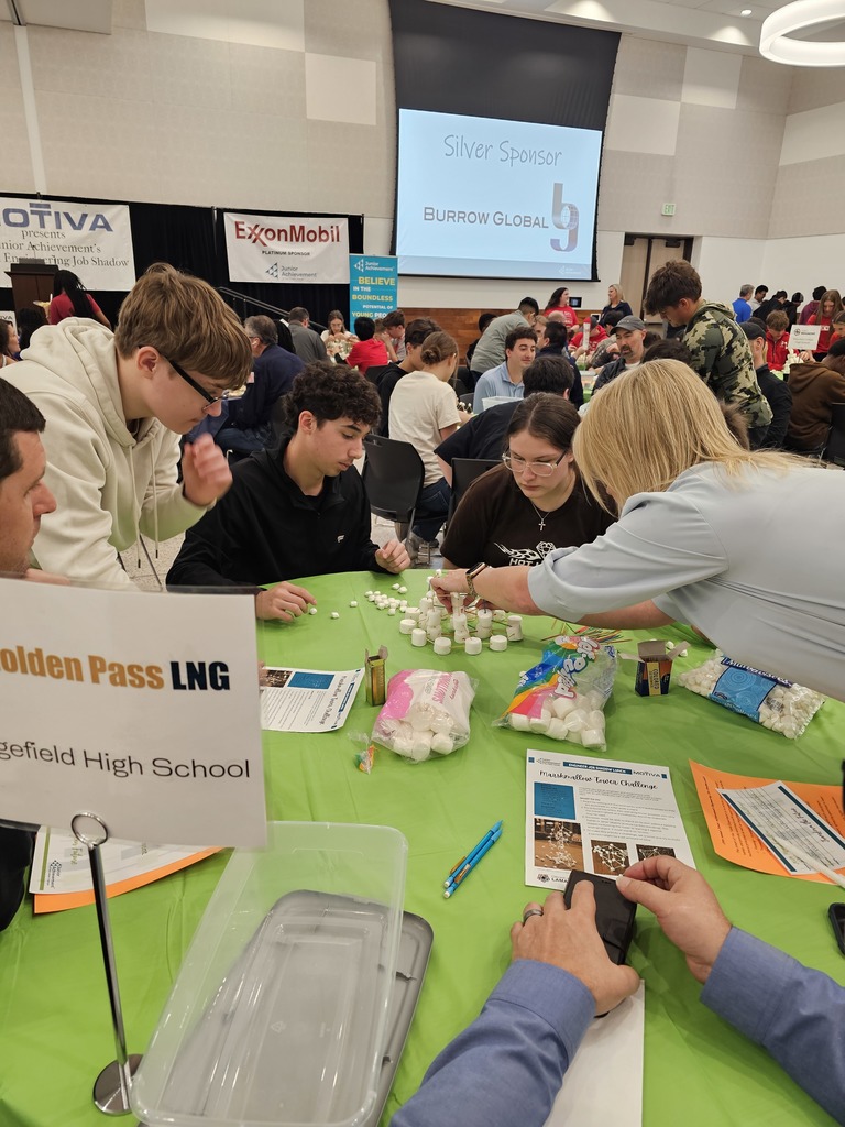 A group of students and adults at a table with science equipment and papers. A sign reads "Golden Pass LNG"