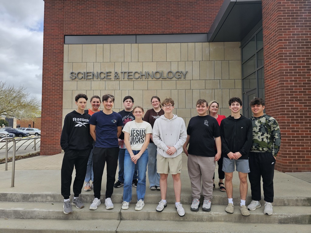 Nine students pose for a picture in front of a brick building labeled "Science and Technology".