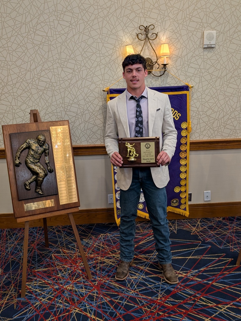 Person in suit and tie holding an award next to a wooden plaque with a football player design.
