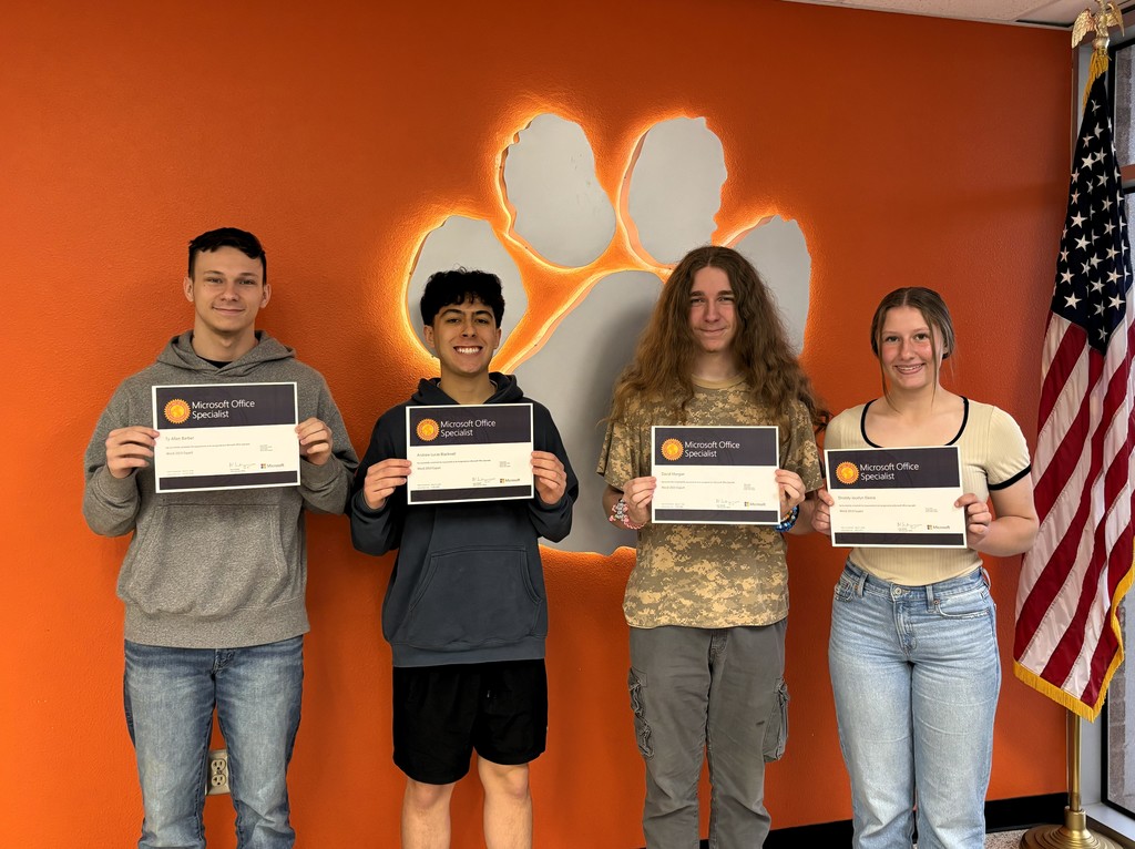 Four students hold certificates in front of an orange wall with a paw print and an American flag.