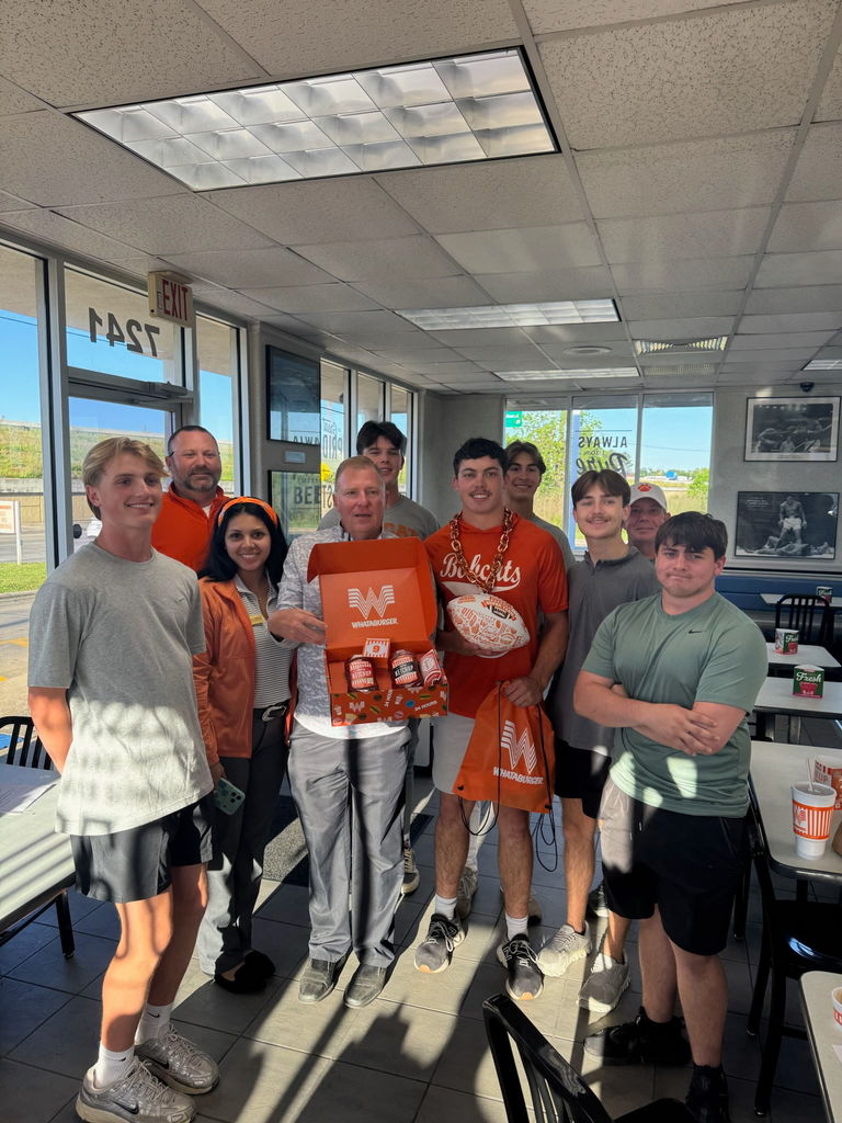 Group of people in orange shirts standing in a cafeteria. One person holds an orange box.