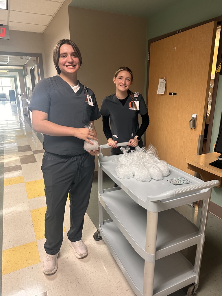 Two people in scrubs stand by a cart with supplies. One holds a bag and smiles.