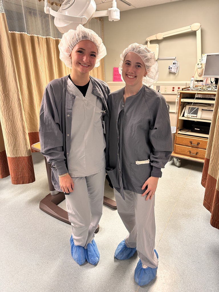 Two women in gray coats and hairnets pose for a photo in a hospital room.