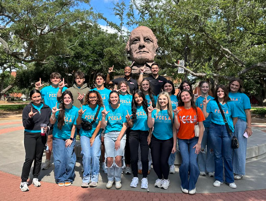 Group of people in matching shirts pose in front of a large statue on campus.