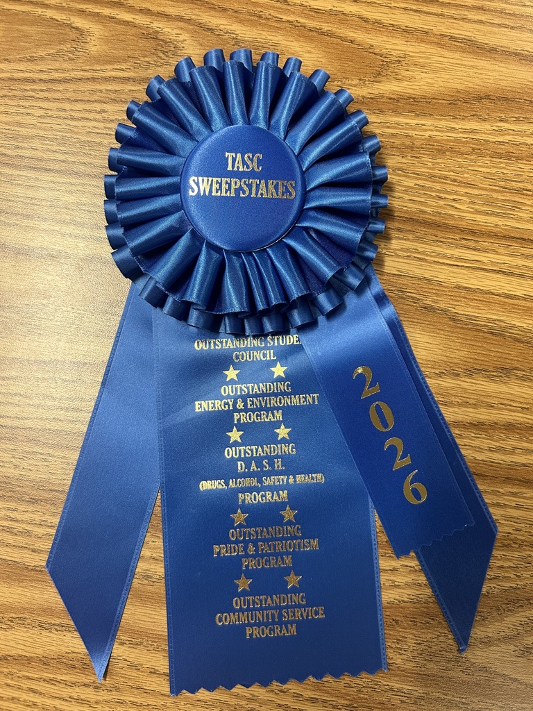 Blue ribbon on a wooden surface. The ribbon reads "TASC SWEEPSTAKES" with a year of "2026" and mentions various programs.