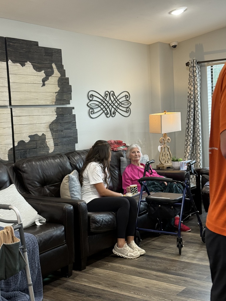 A living room with a woman using a walker and a girl sitting on a couch. A lamp on a table.
