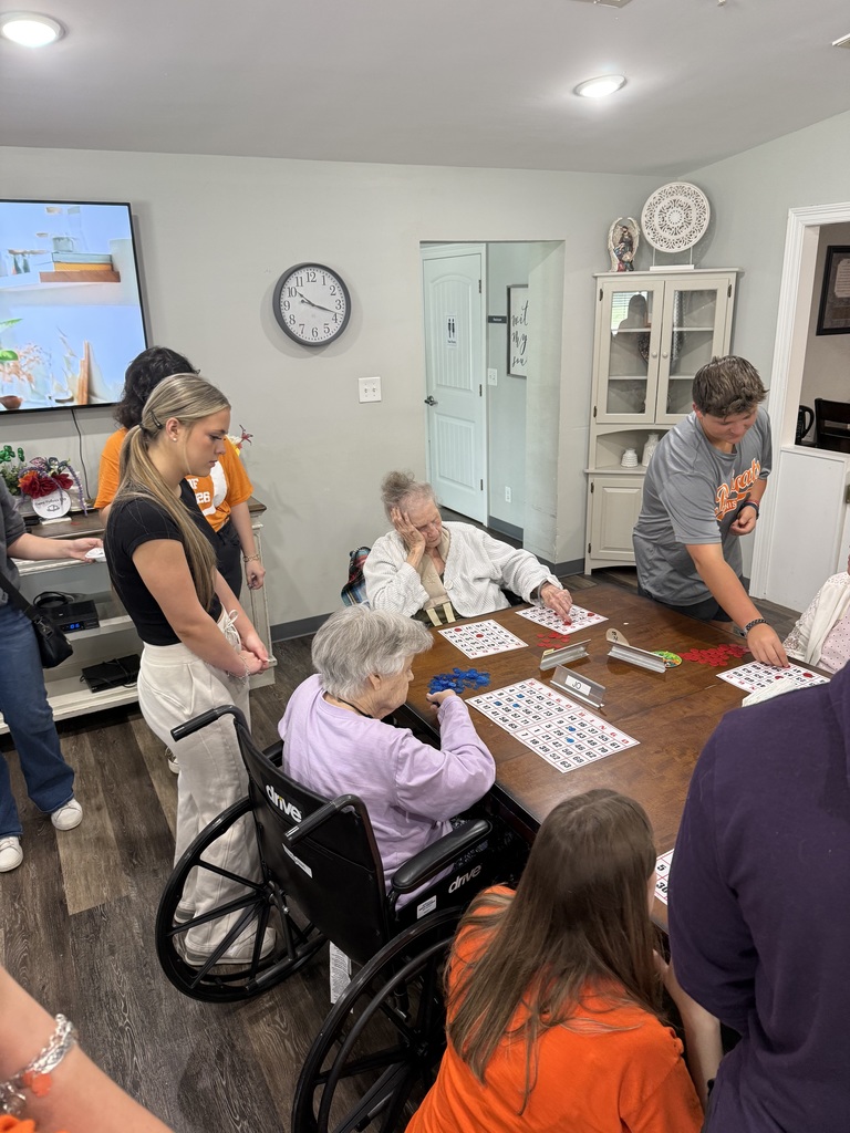 People play bingo in a room, one person in a wheelchair, with a table full of bingo cards.