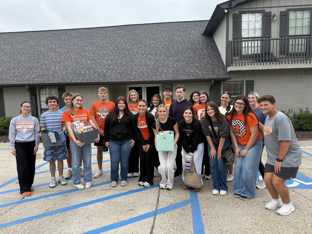 Group of students in jeans and orange shirts holding boxes.