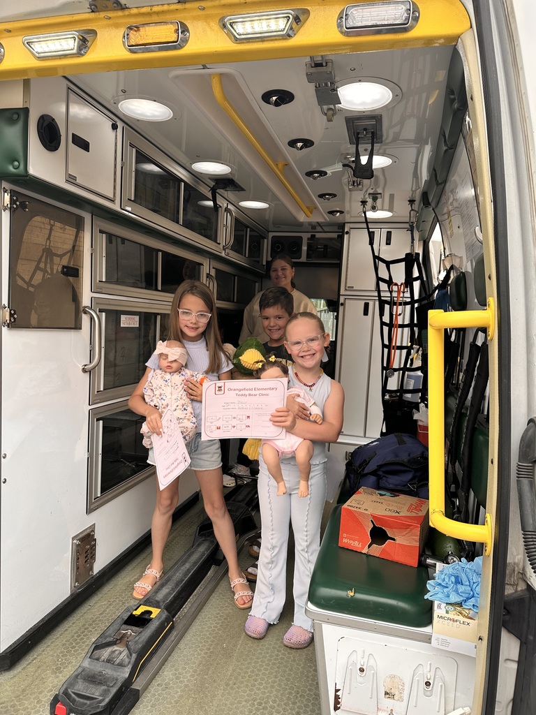 Three kids hold stuffed animals in the back of an ambulance with yellow accents.