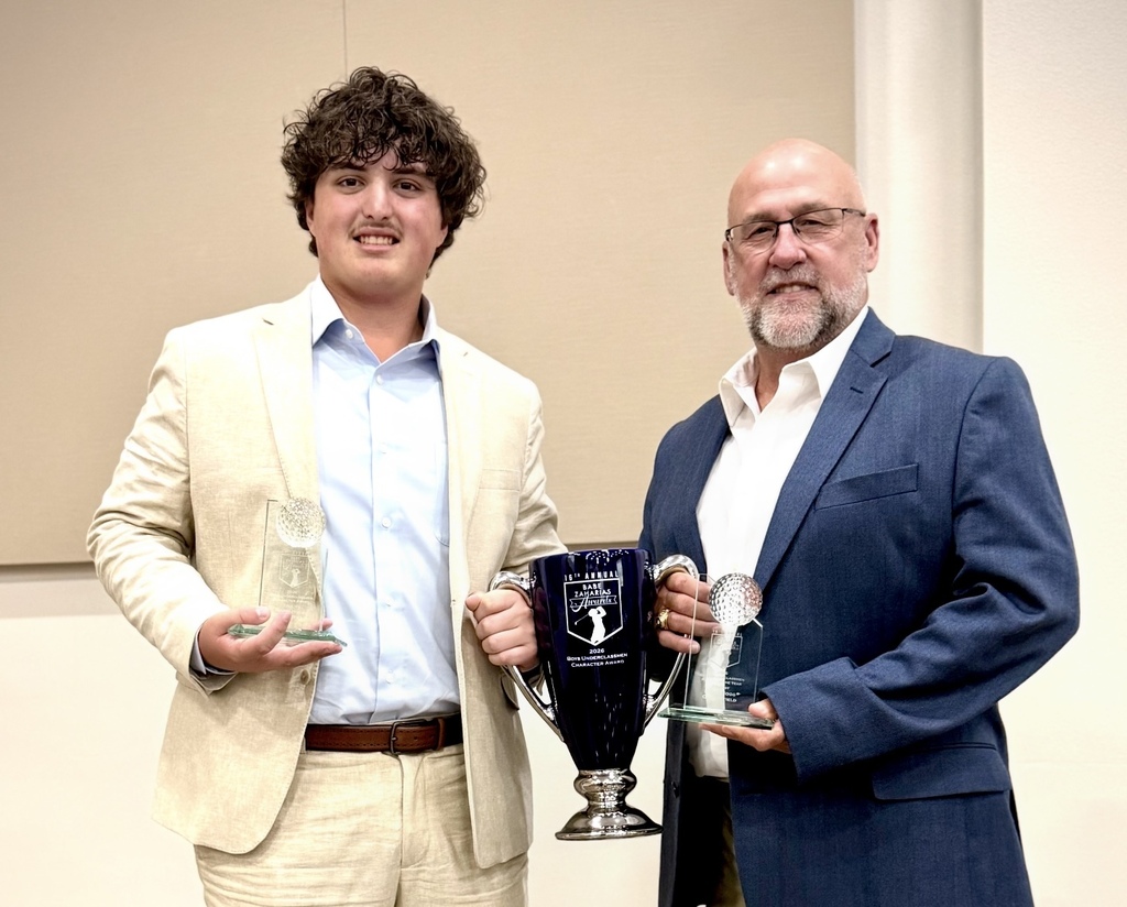 Two men in suits, one holding a trophy, smile. One man holds a trophy and a smaller award.