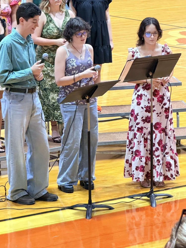 Three students standing at microphones in dress clothes and dresses  