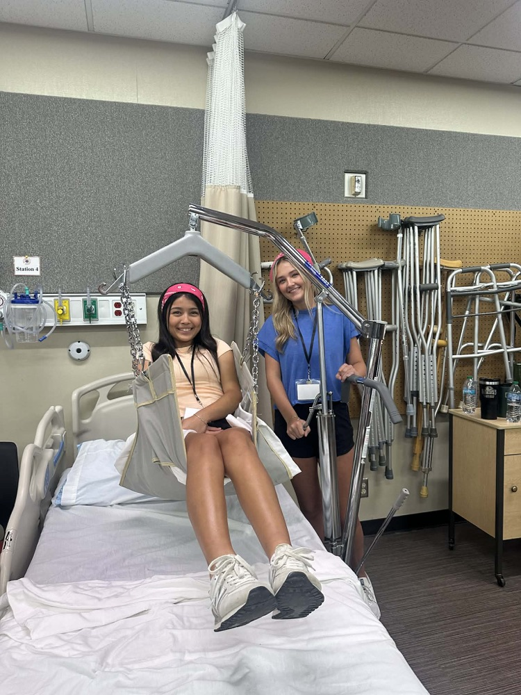 student in a hospital bed with legs in sling