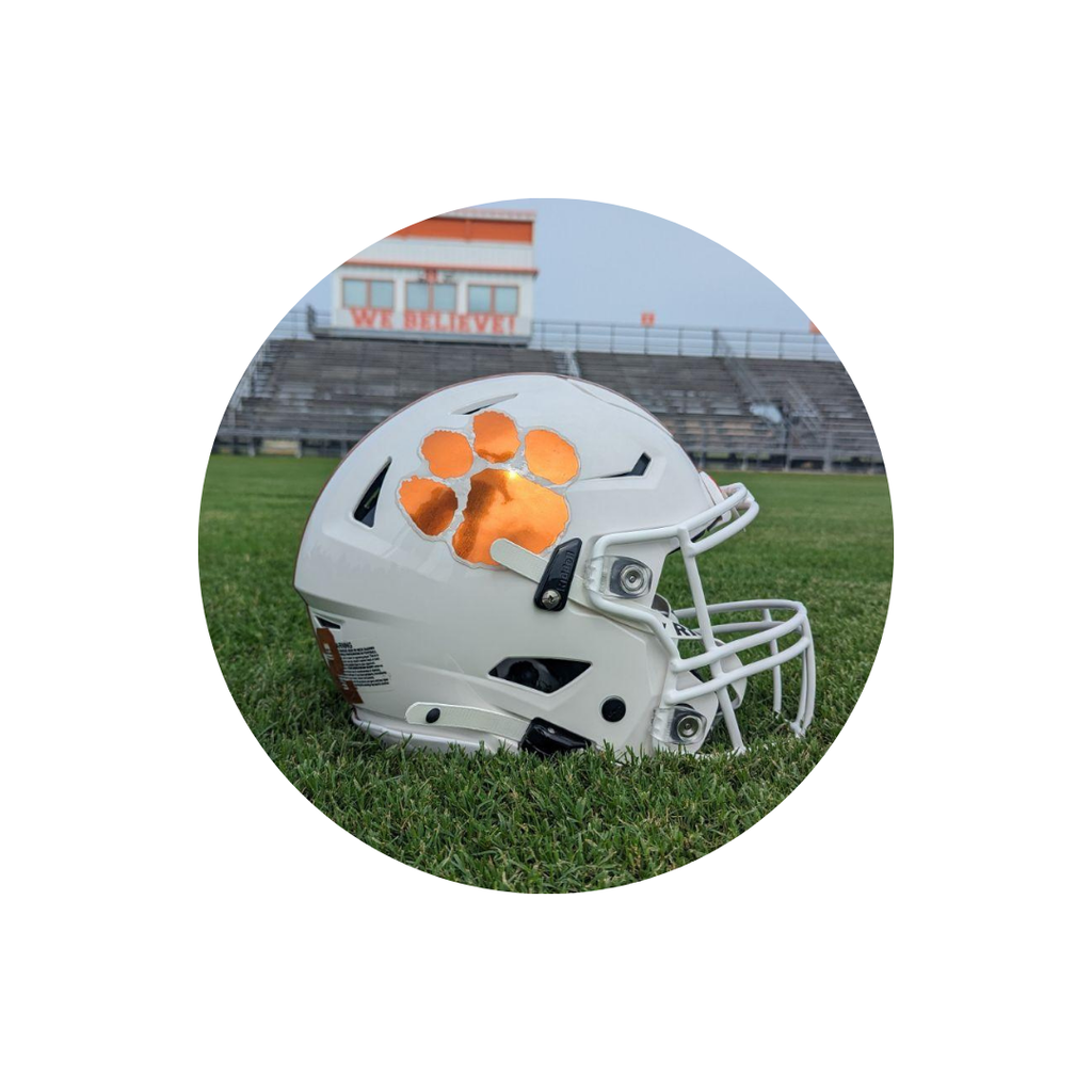 Helmet with a reflective orange paw print on a grass field, stadium and bleachers in the background.